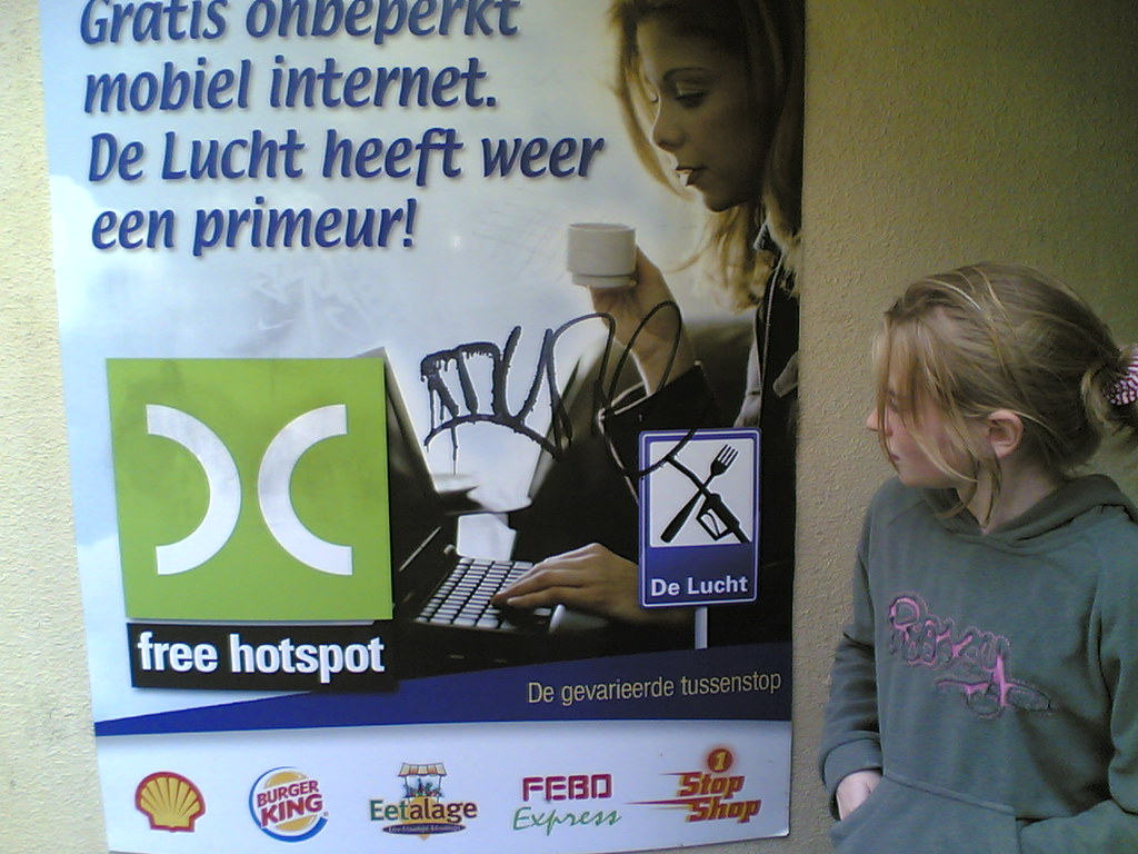 A Dutch 'free hotspot' advertising poster using the warchalking open-node symbol as its logo, next to graffiti of the mark scrawled on a laptop